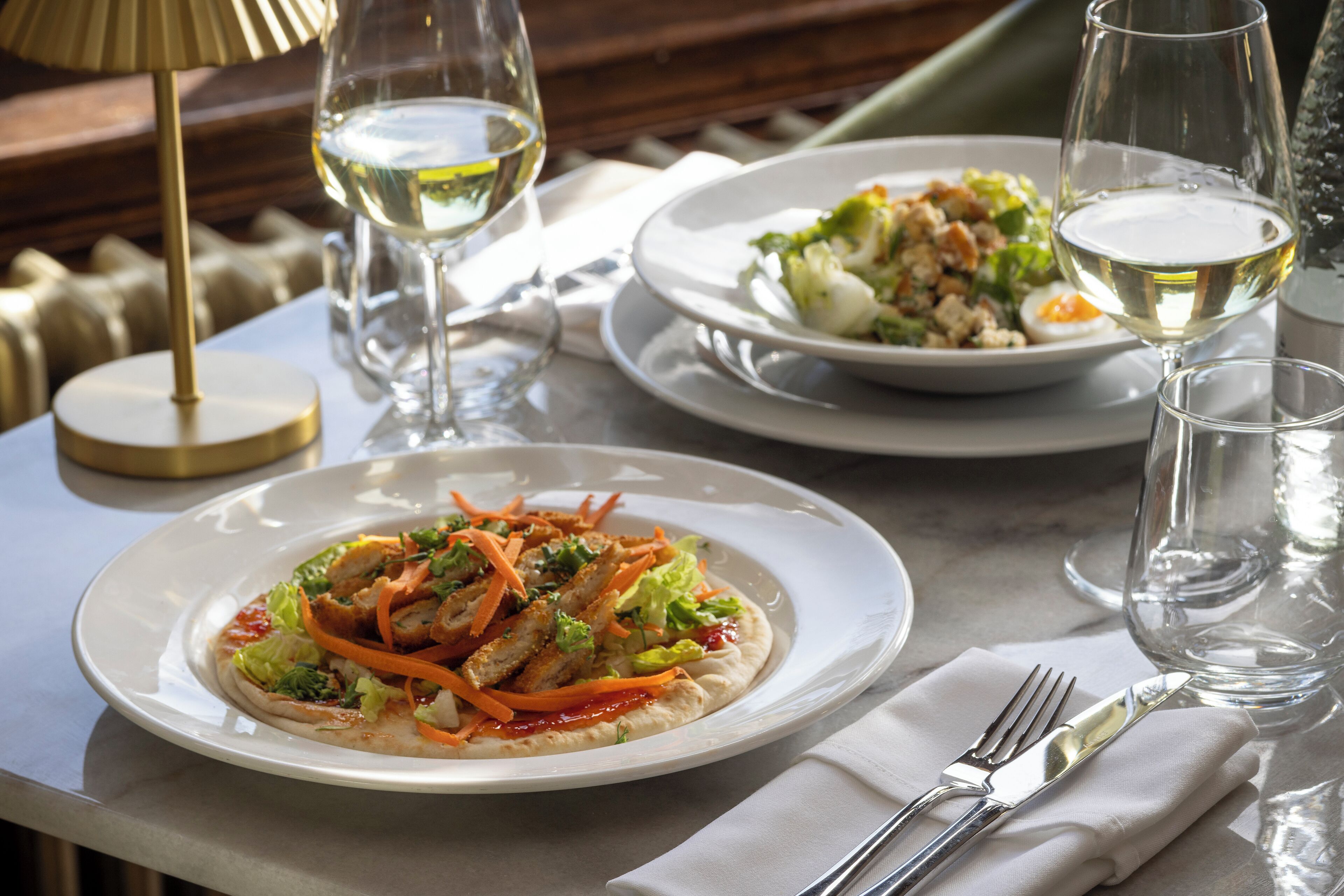 A dining table with plates of food, wine glasses, and cutlery.