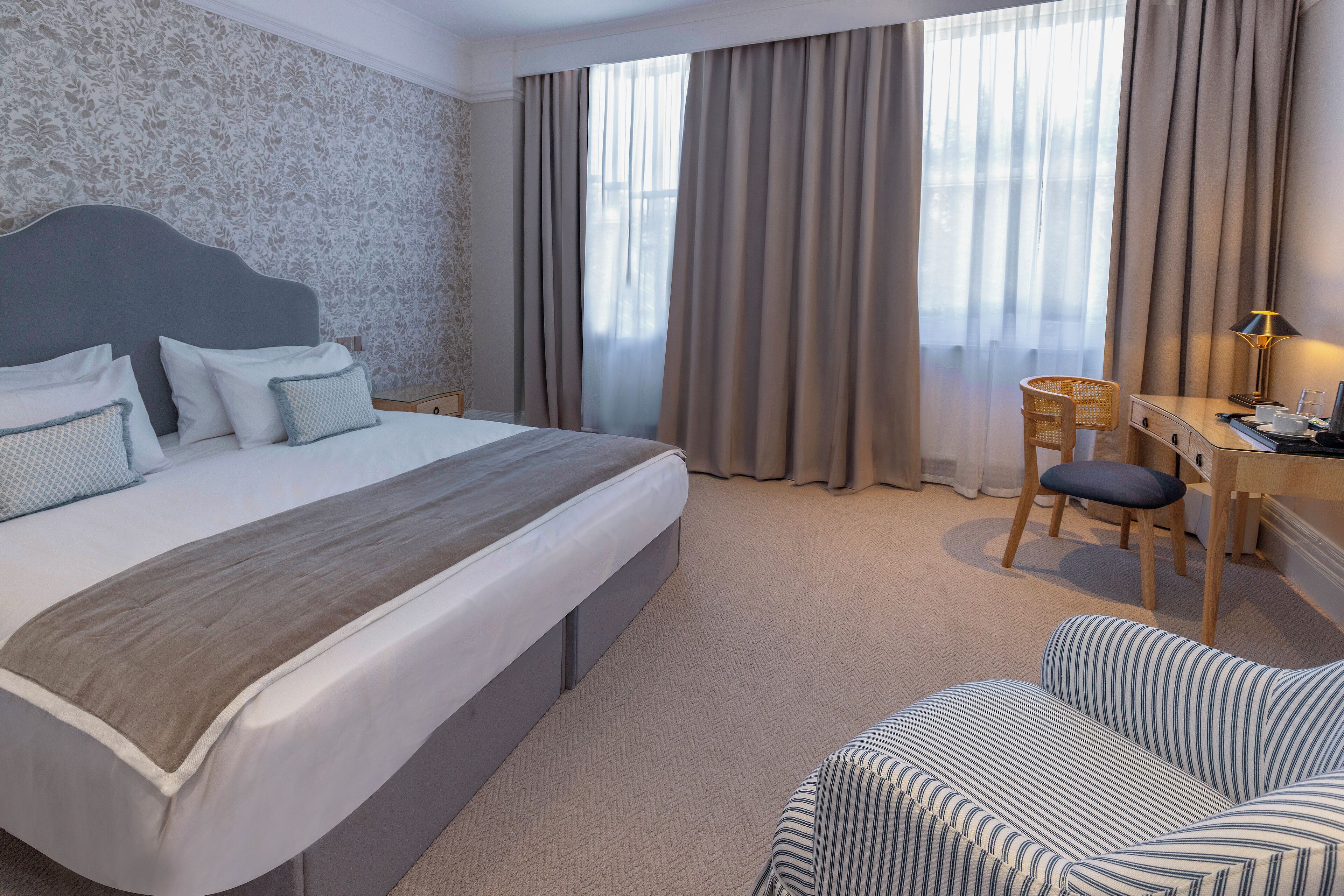 A hotel room with a large bed, a desk, a chair, and a sofa.