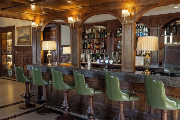 A bar area with wooden paneling, green bar stools, and a well-stocked liquor shelf.