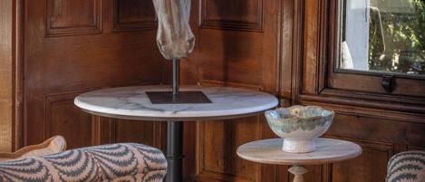 A room with a wooden paneled wall, a round table with a bowl, patterned chairs, and a head sculpture.