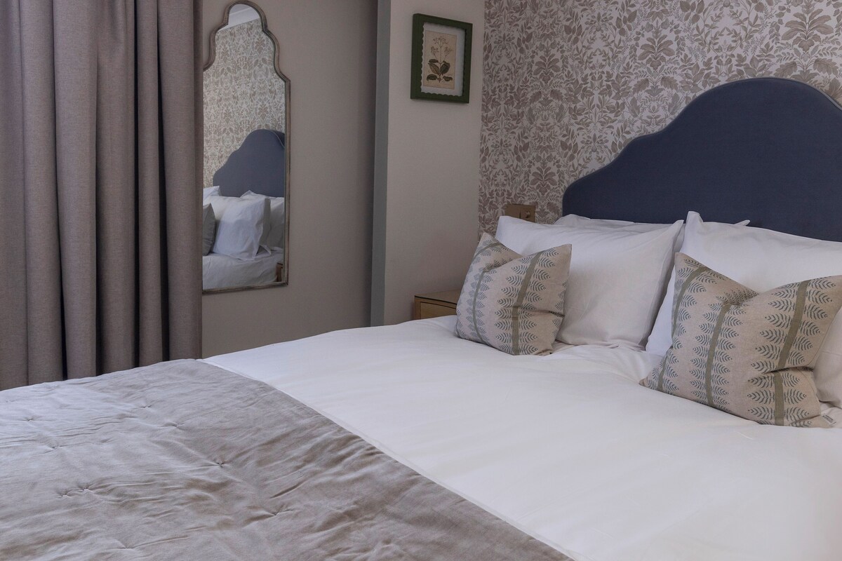 A neatly made bed with a headboard, a mirror, and patterned wallpaper.