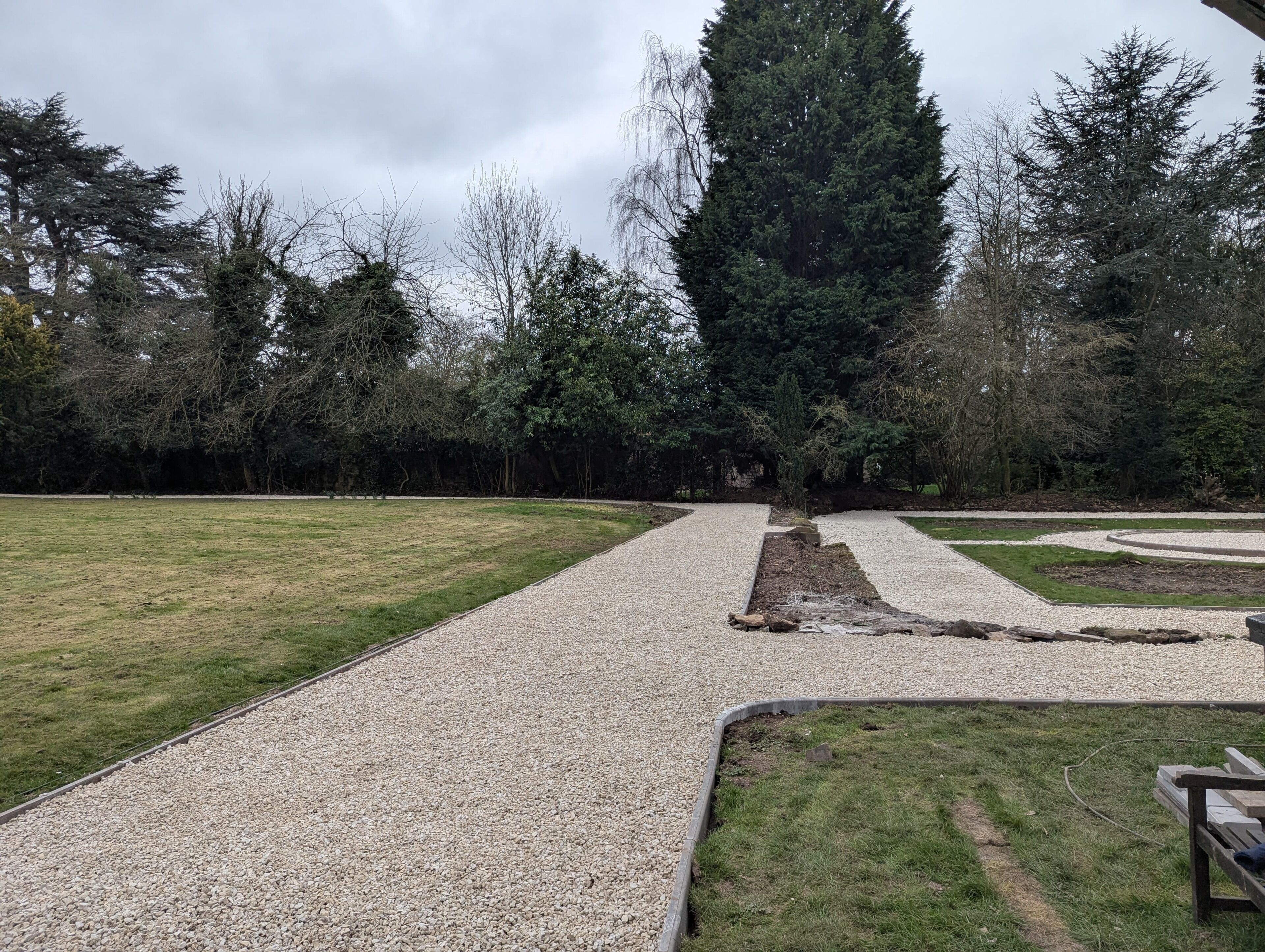 A park with gravel paths, green grass, and trees.