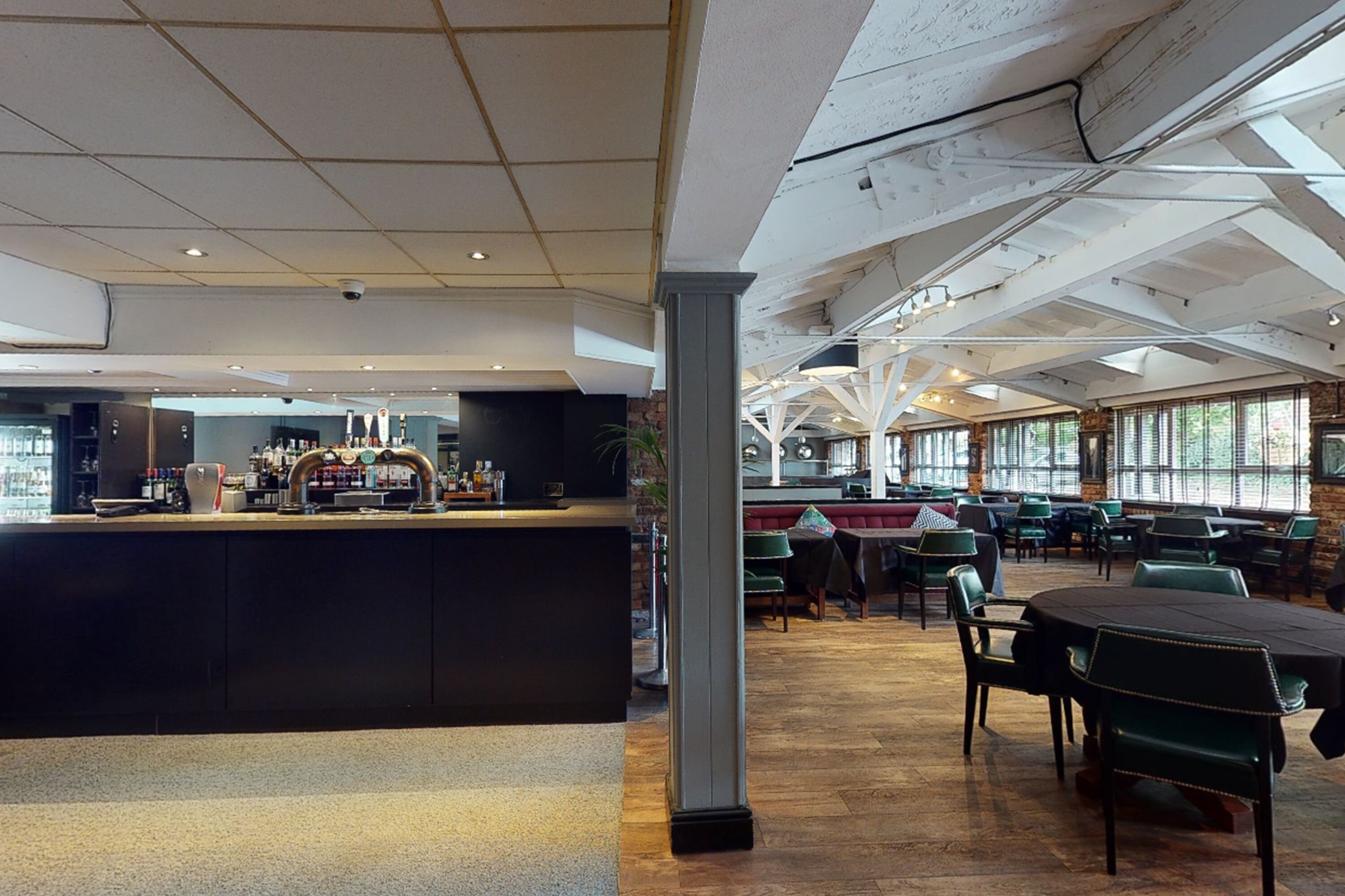 A spacious indoor area with a bar counter, tables, and chairs, featuring a high ceiling and large windows.