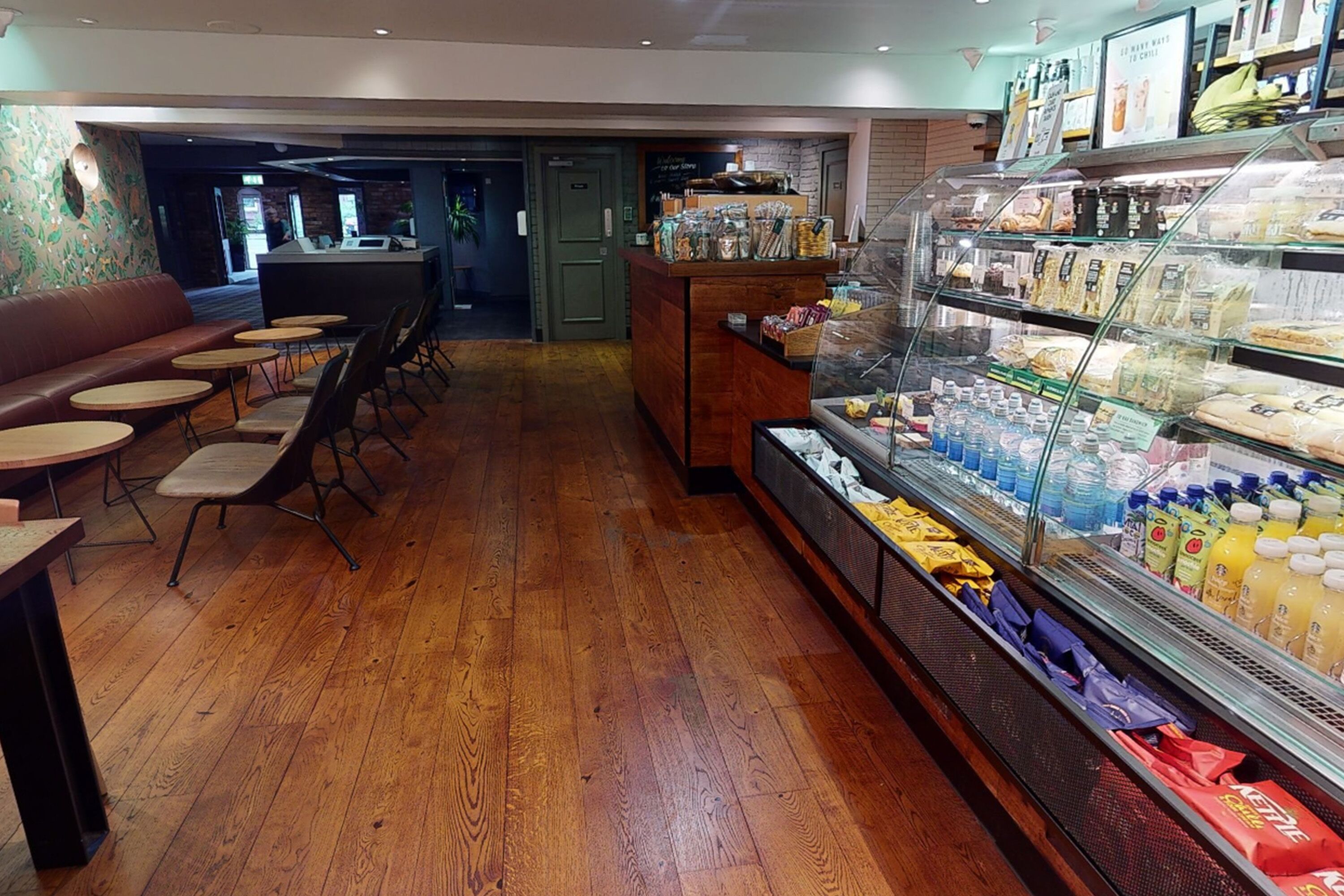 A café with wooden flooring, a counter with snacks, and a display case with beverages.