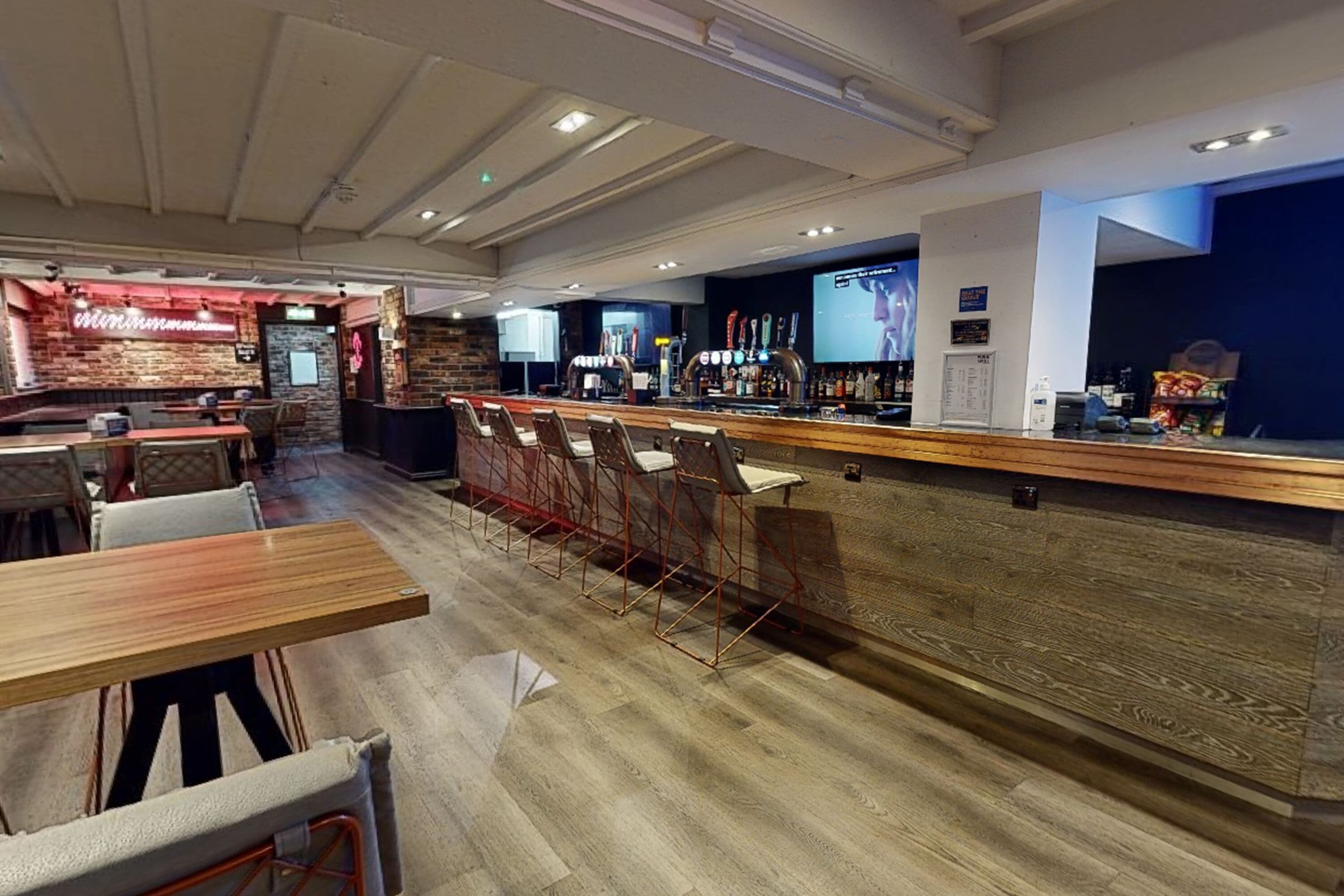 Zona de bar con taburetes, mesas y una barra con carta.