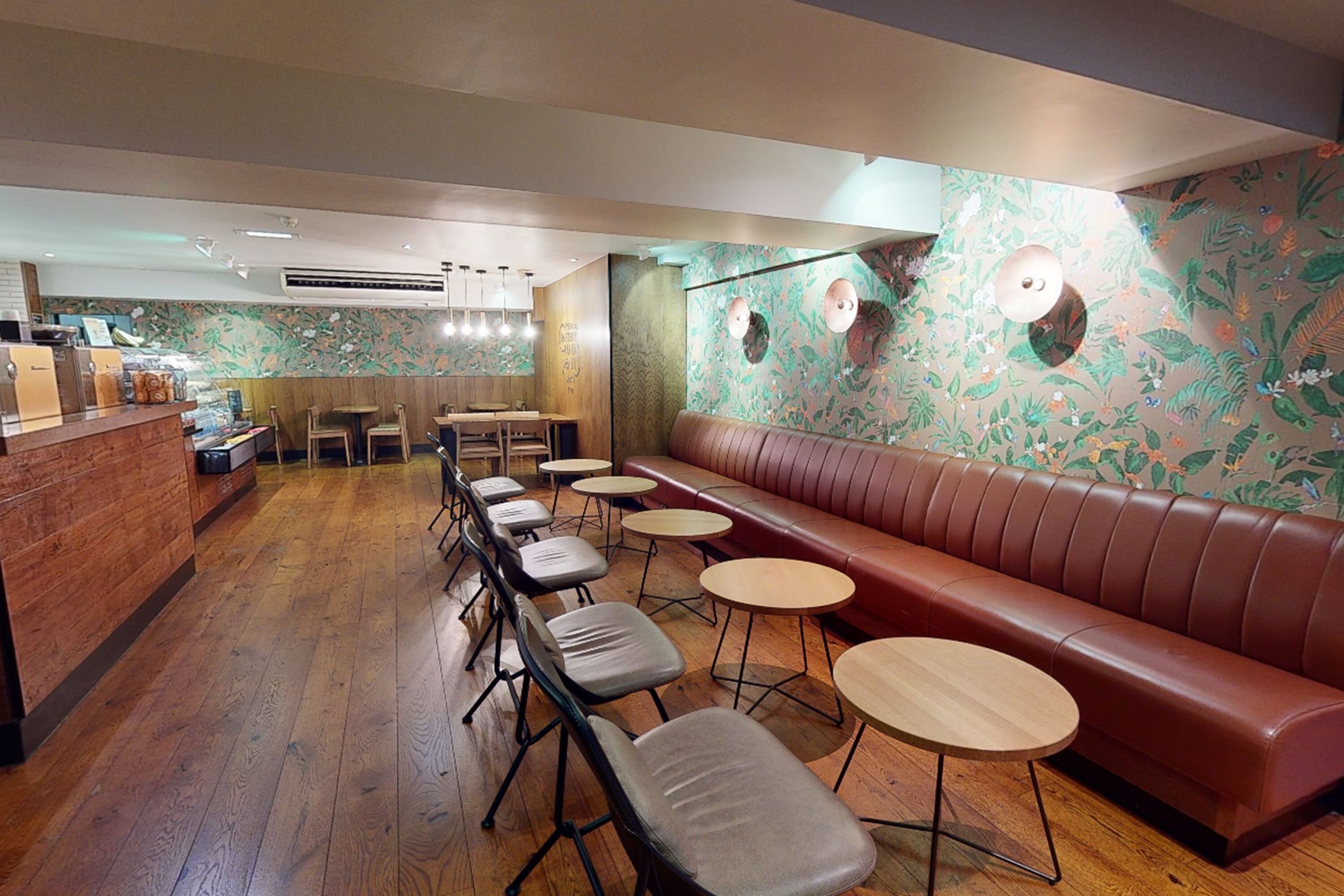 A restaurant interior with a wooden floor, a long red leather booth, multiple tables, and chairs.