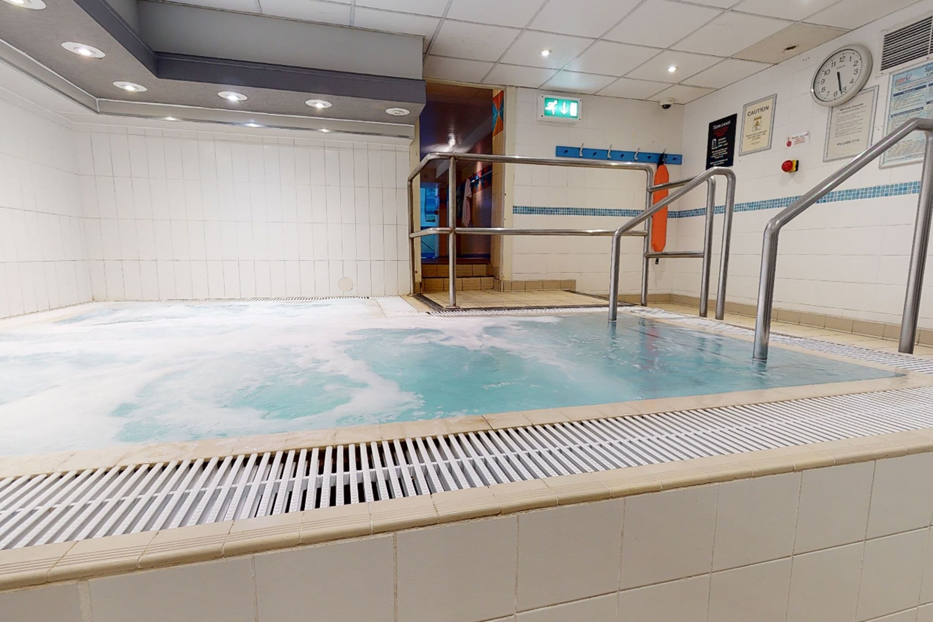 A swimming pool with a metal ladder and a tiled deck.