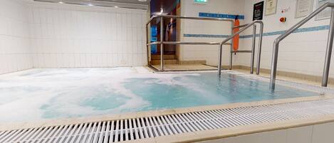 A swimming pool with a metal ladder and a tiled deck.
