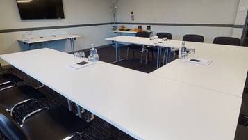 A conference room with a long table, chairs, a projector screen, and a small table with fruits and water bottles.