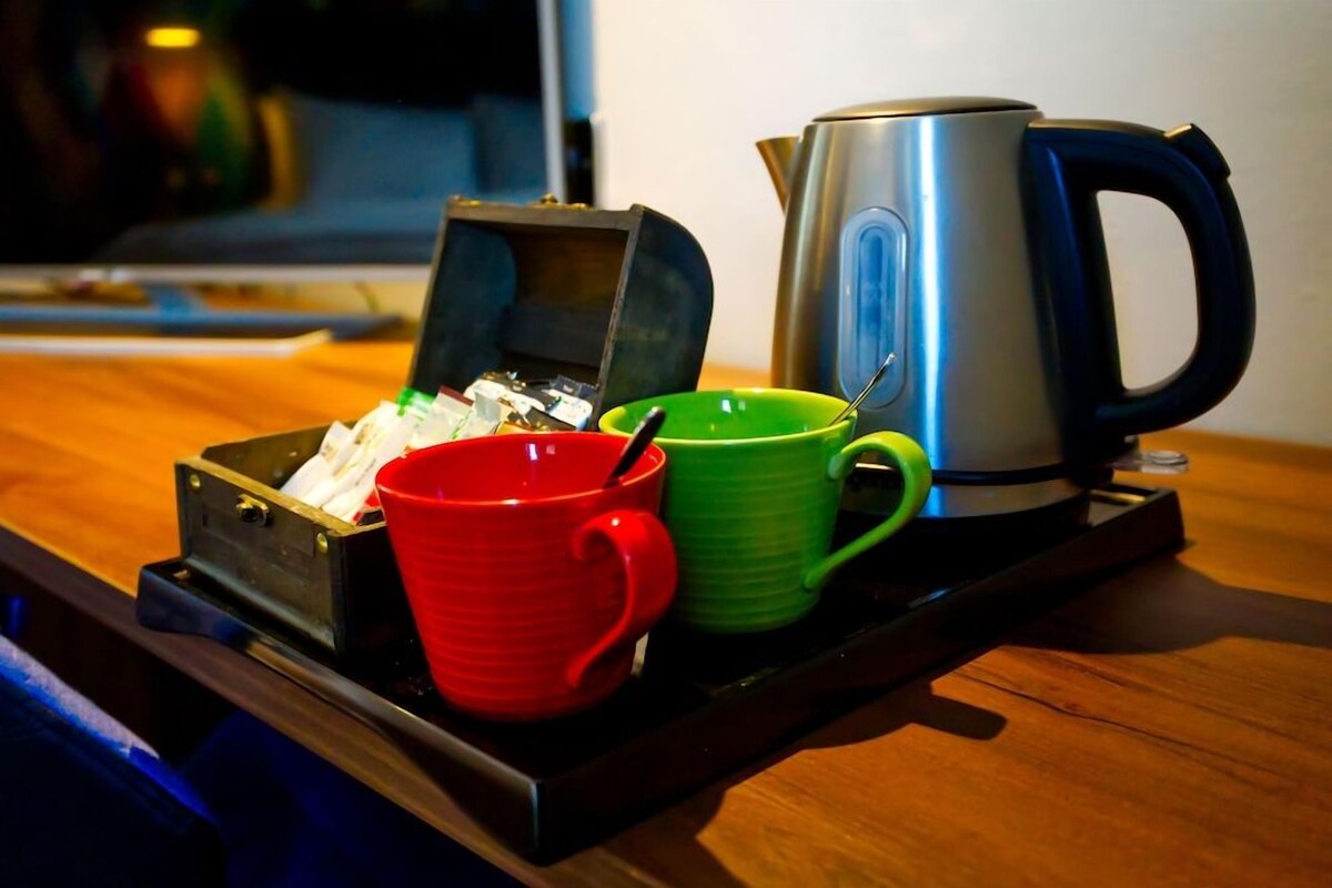 A tray with a red mug, a green mug, and a silver kettle on a wooden table.