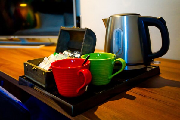 Una bandeja con un hervidor plateado, una taza roja y una taza verde sobre una mesa de madera.