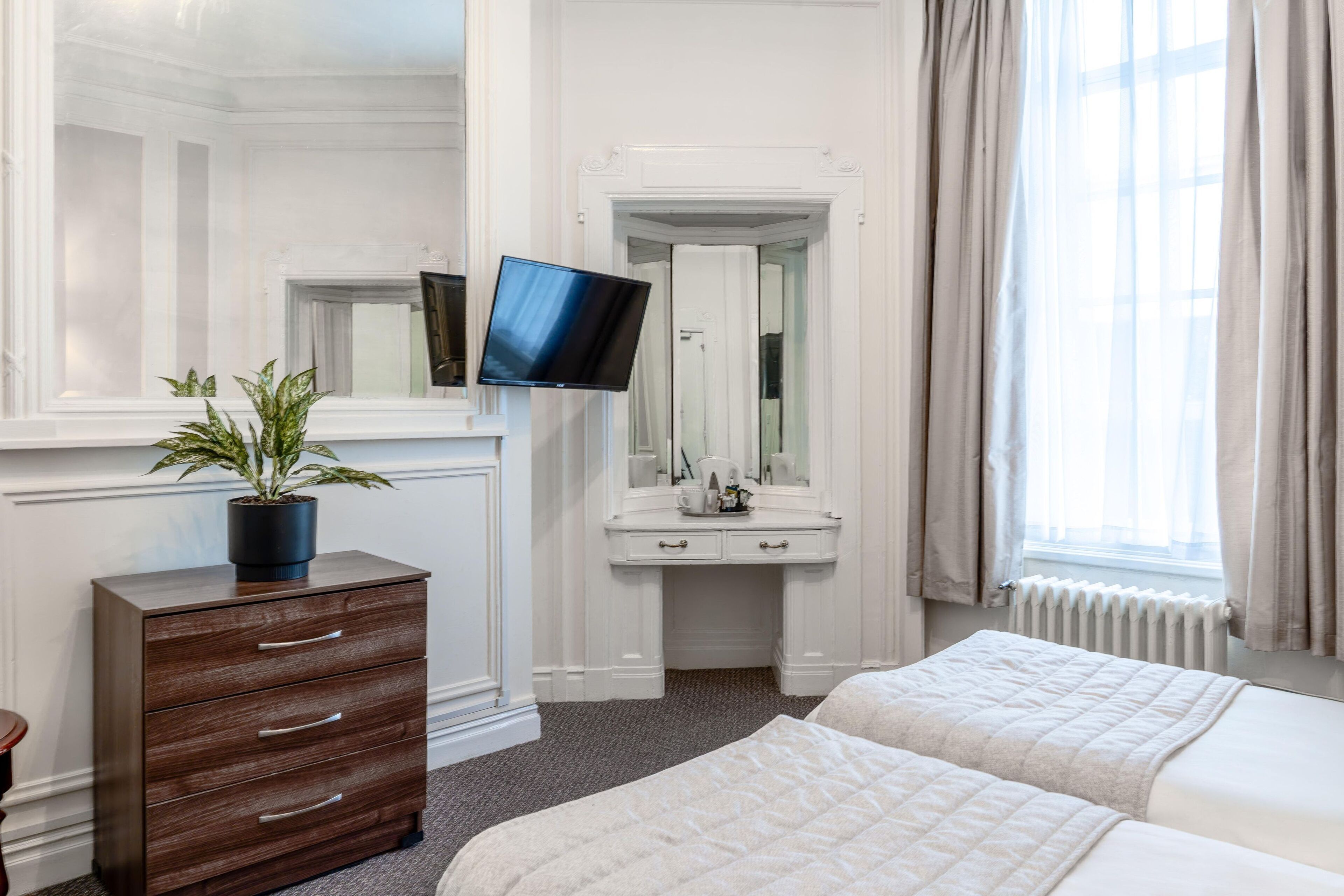 A hotel room with a bed, a dresser, a television, a mirror, and a window with curtains.