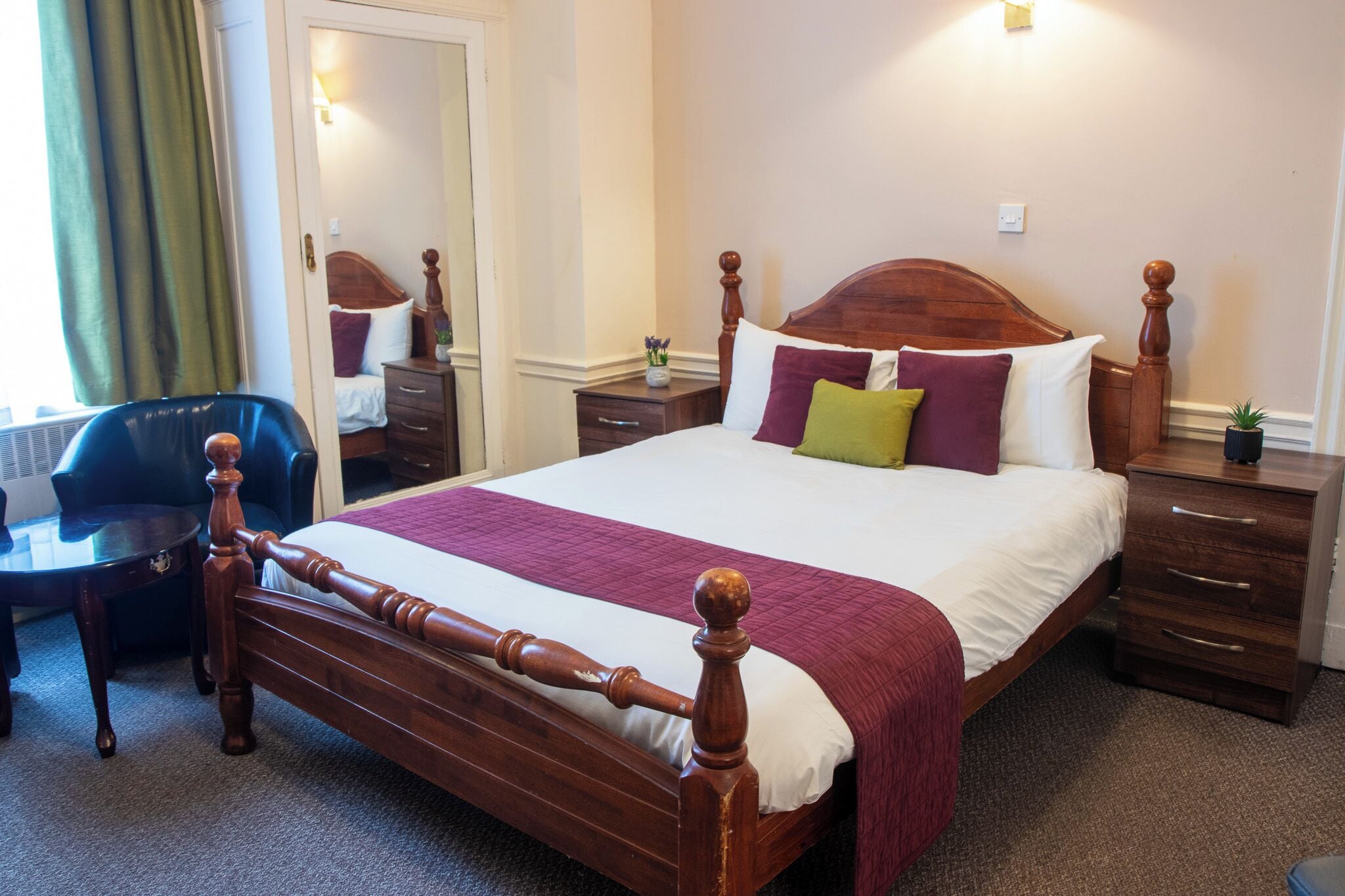 A neatly arranged hotel room with a wooden bed, a bedside table, a chair, and a small desk.