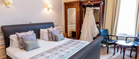 A hotel room with a large bed, a sitting area with a table and chairs, a wardrobe, and a mirror.