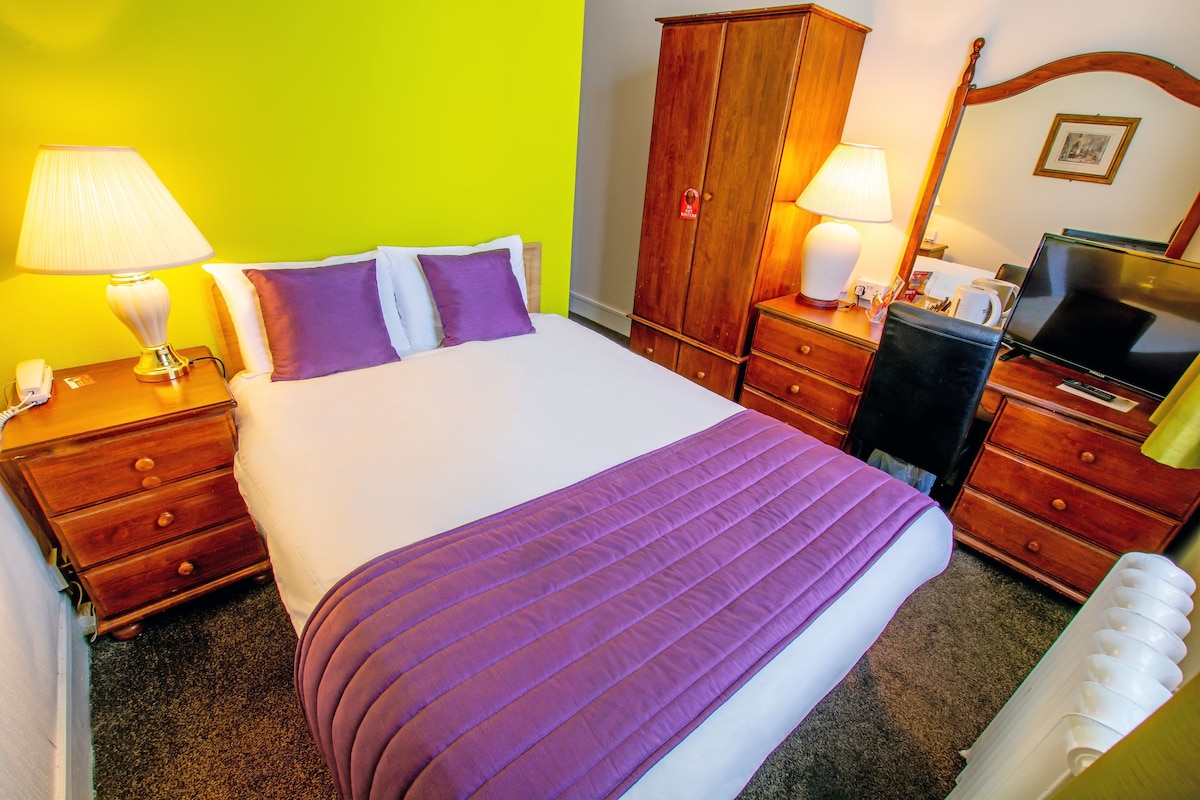 A hotel room with a bed, a wardrobe, a desk with a lamp, a television, and a telephone.