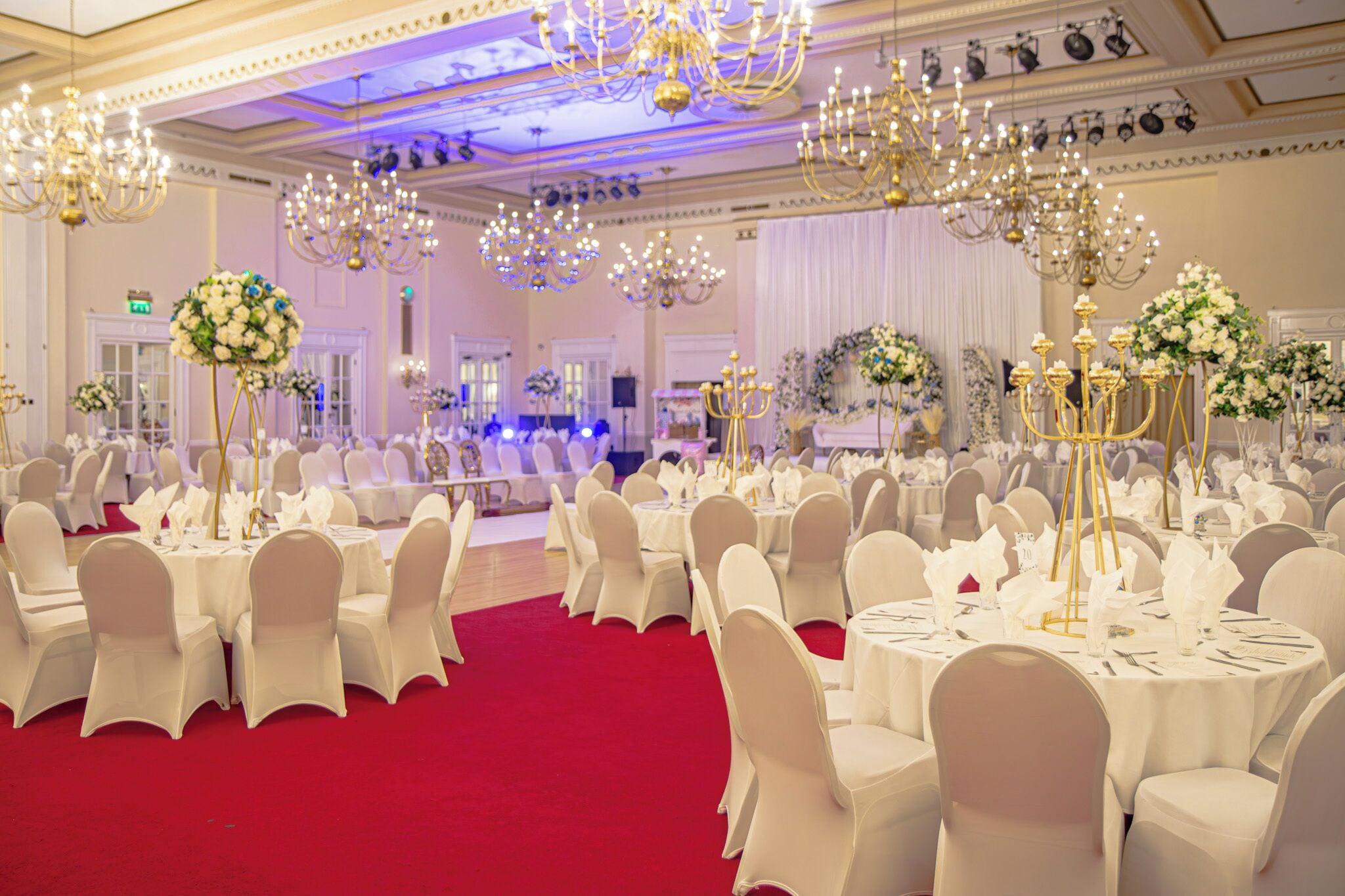 A banquet hall with round tables, white chairs, and chandeliers.