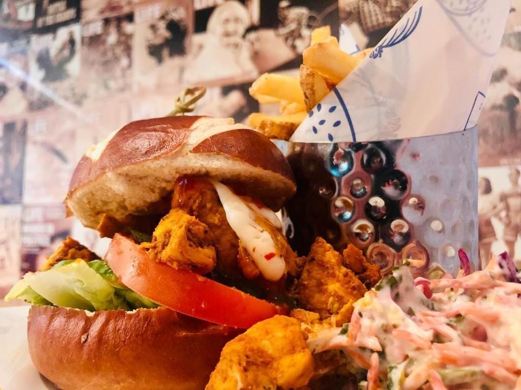 Un sándwich de pollo frito, un pan, lechuga, tomate y una guarnición de ensalada de col.