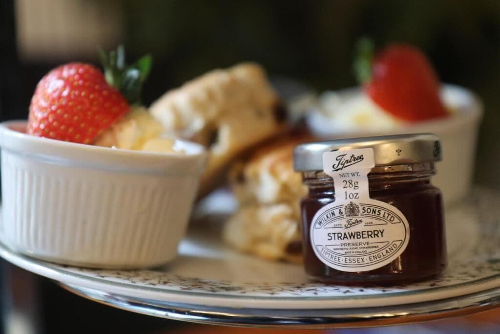 A dessert plate with a bowl of custard, a strawberry, and a jar of strawberry preserve.