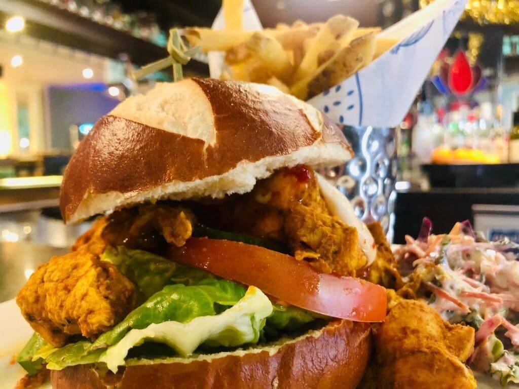 Primer plano de un sándwich de pollo con lechuga y tomate, acompañado de papas fritas.