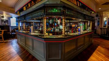 A bar with a high counter, multiple shelves with bottles, and a wooden floor.