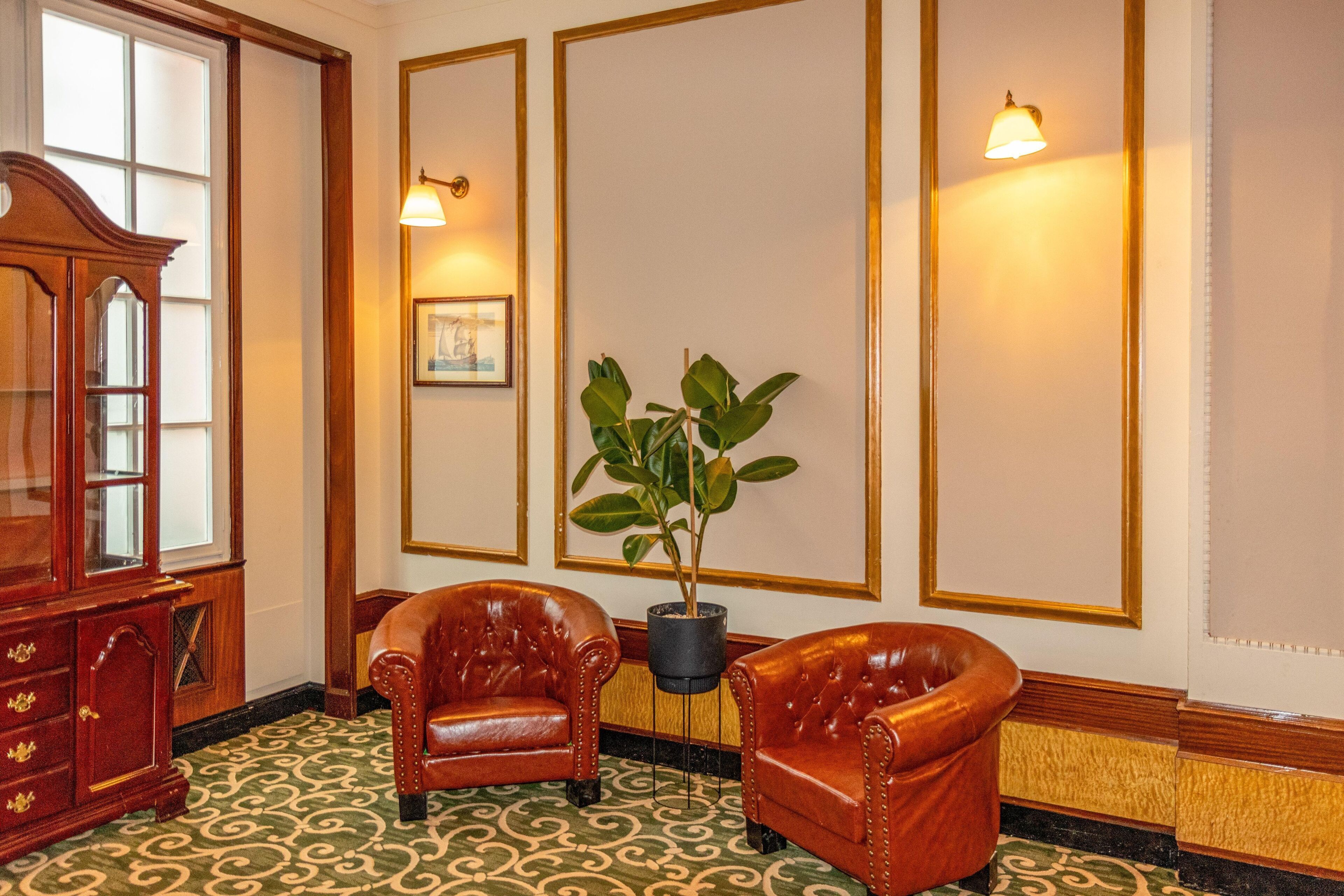 A room with two leather armchairs, a wooden cabinet, and a potted plant.