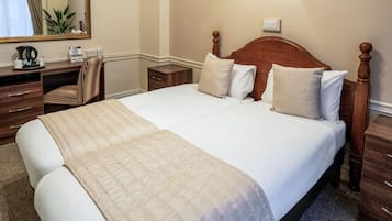 A neatly made bed with a wooden headboard, a bedside table, a chair, and a desk with a mirror and some items on it.
