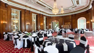 Un salón de banquetes con mesas redondas, sillas blancas y negras, candelabros y suelo de moqueta roja.