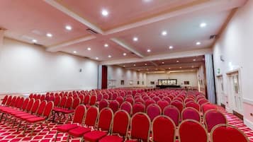 A large conference room with rows of red chairs and a carpeted floor.