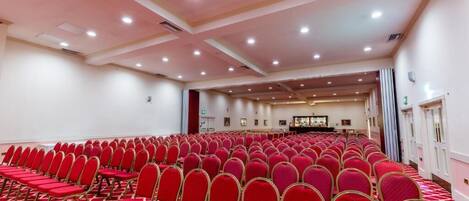 Un amplio salón de conferencias con filas de sillas rojas y suelo alfombrado.
