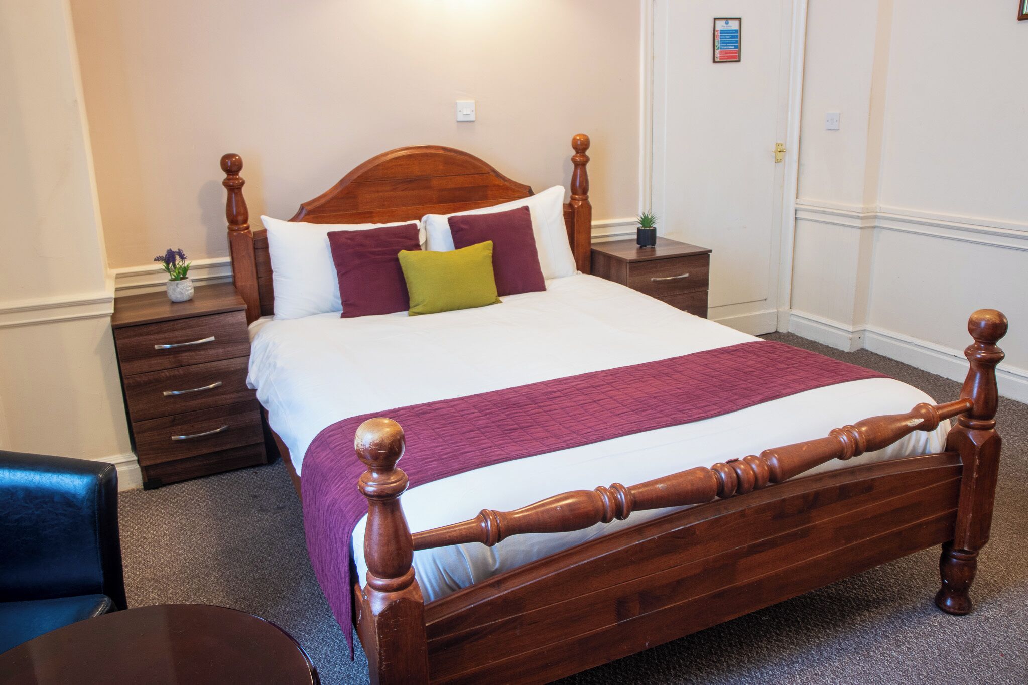 A neatly made bed with a wooden headboard, a bedside table with a lamp, and a small potted plant.