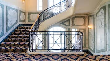 Una imponente escalera con barandilla de metal negro, paredes de mármol y alfombra estampada.