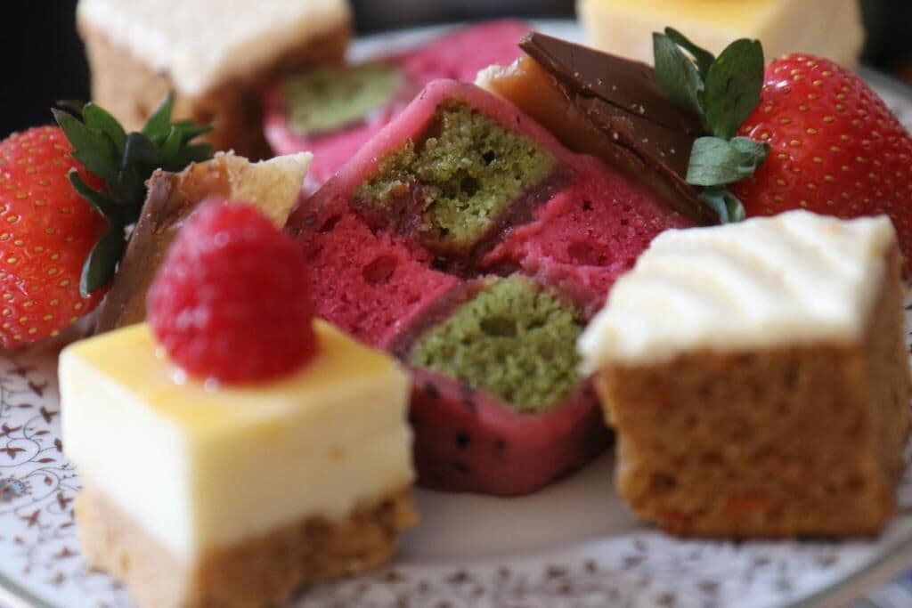 A variety of desserts on a plate, including a slice of cake with a green filling, a piece of cheesecake, and a chocolate bar.
