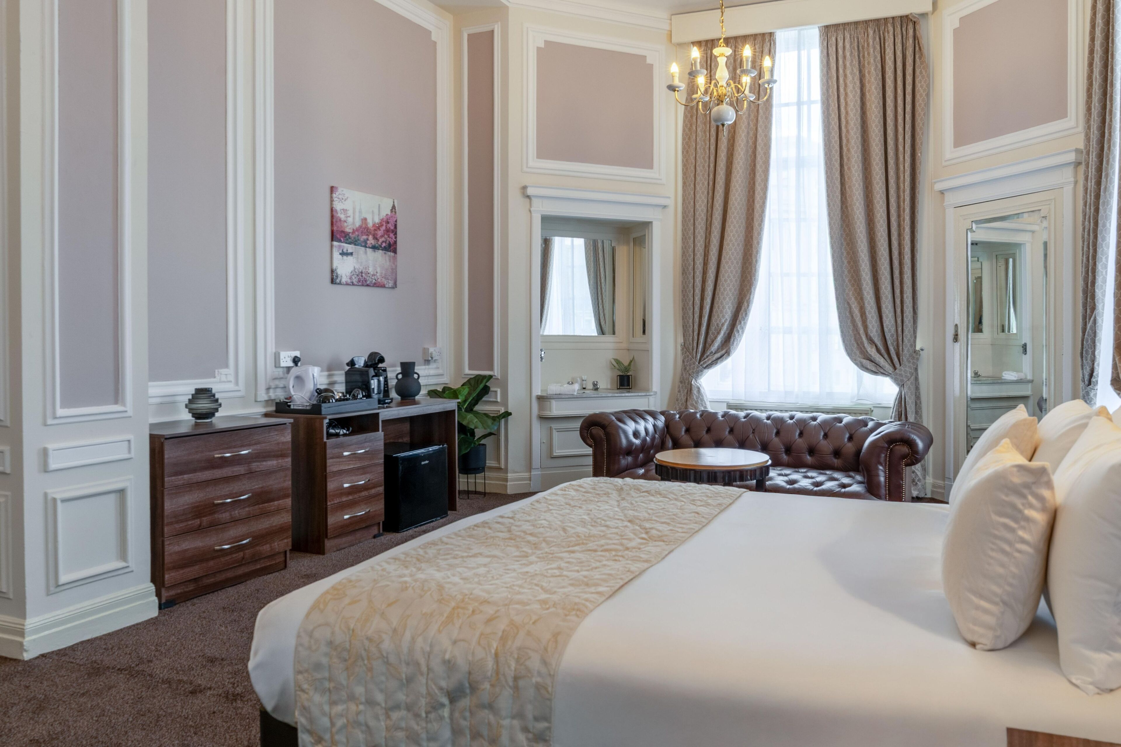 A hotel bedroom with a large bed, a vanity with a mirror, a seating area with a sofa, and a chandelier.