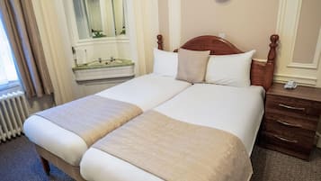 Una cama doble con dos almohadas, cabecera de madera, mesita de noche con lámpara y espejo sobre el aparador.