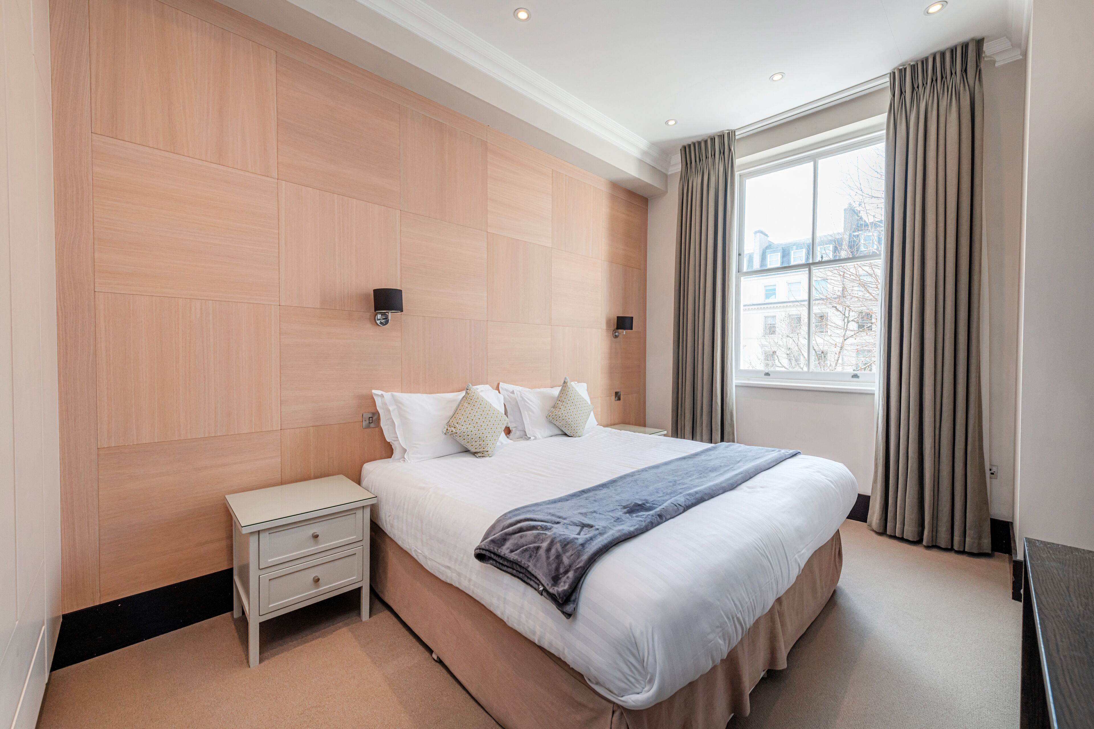 A hotel room with a large bed, a nightstand, and a window with curtains.