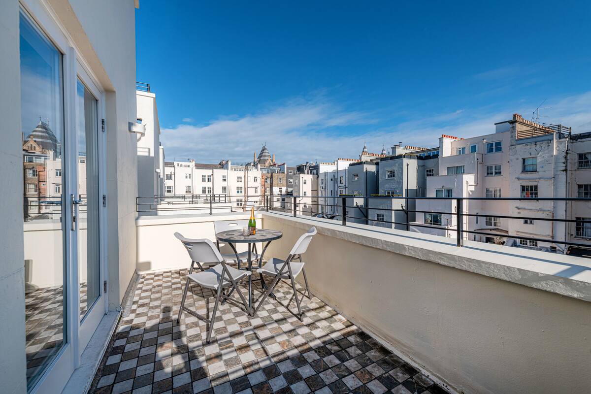 A balcony with a checkered floor, a table with chairs, and a bottle of champagne.