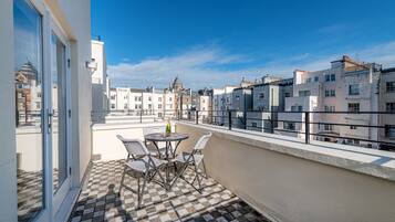 A balcony with a checkered floor, a table with chairs, and a bottle of champagne.