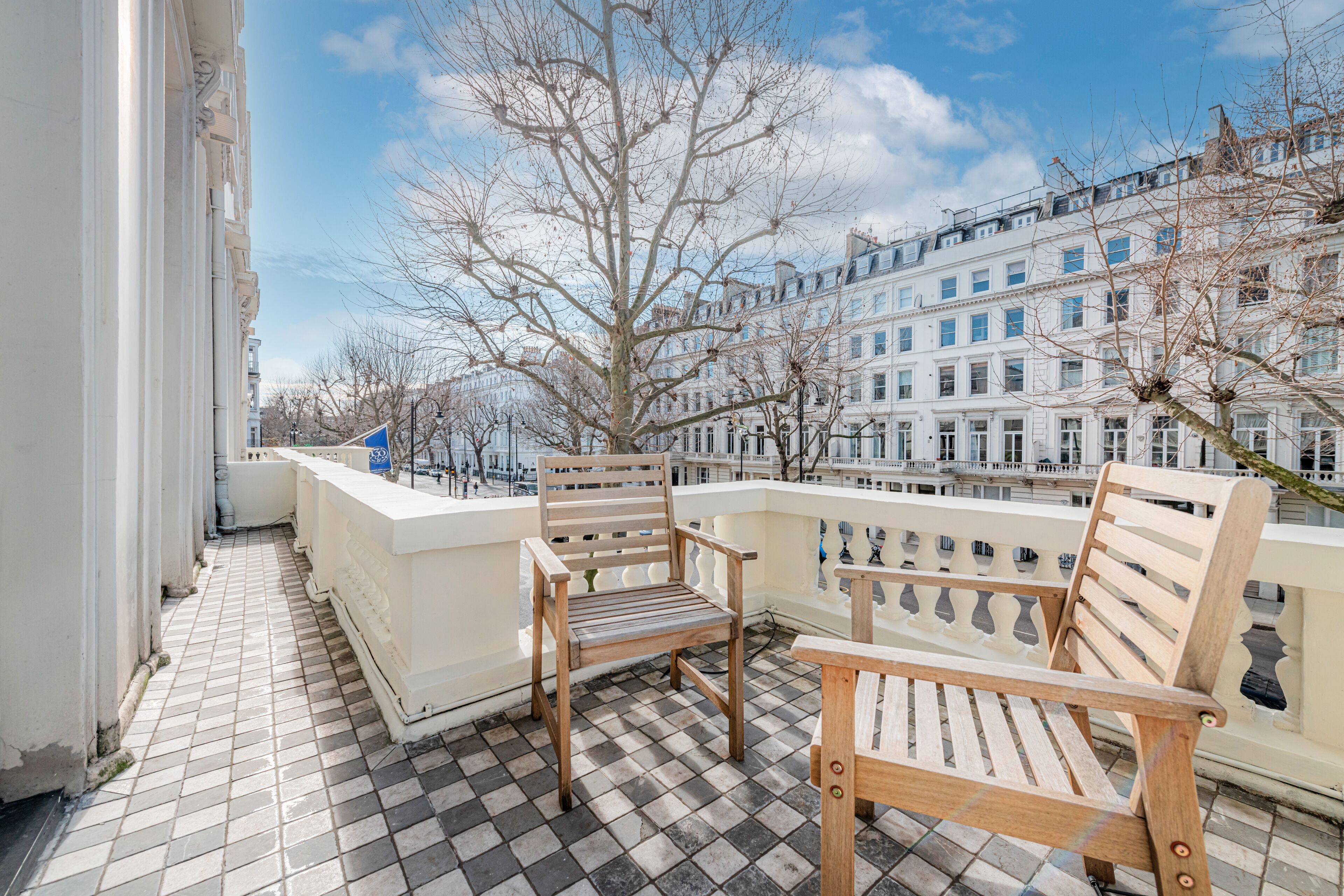 A balcony with two wooden benches, a tiled floor, and a view of buildings and trees.
