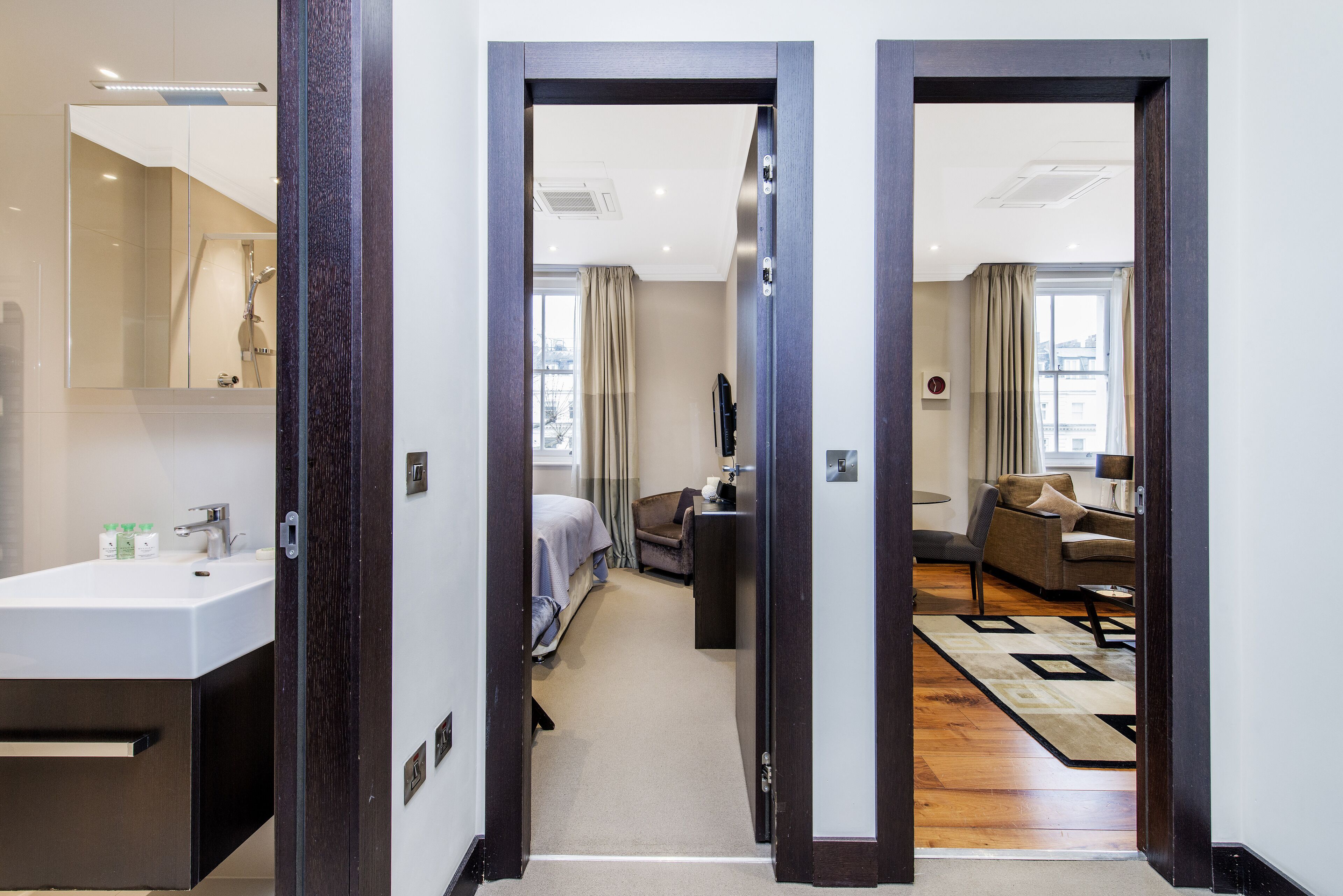 A hotel room with a bathroom, a bed, a sofa, and a living area with a view of the city.