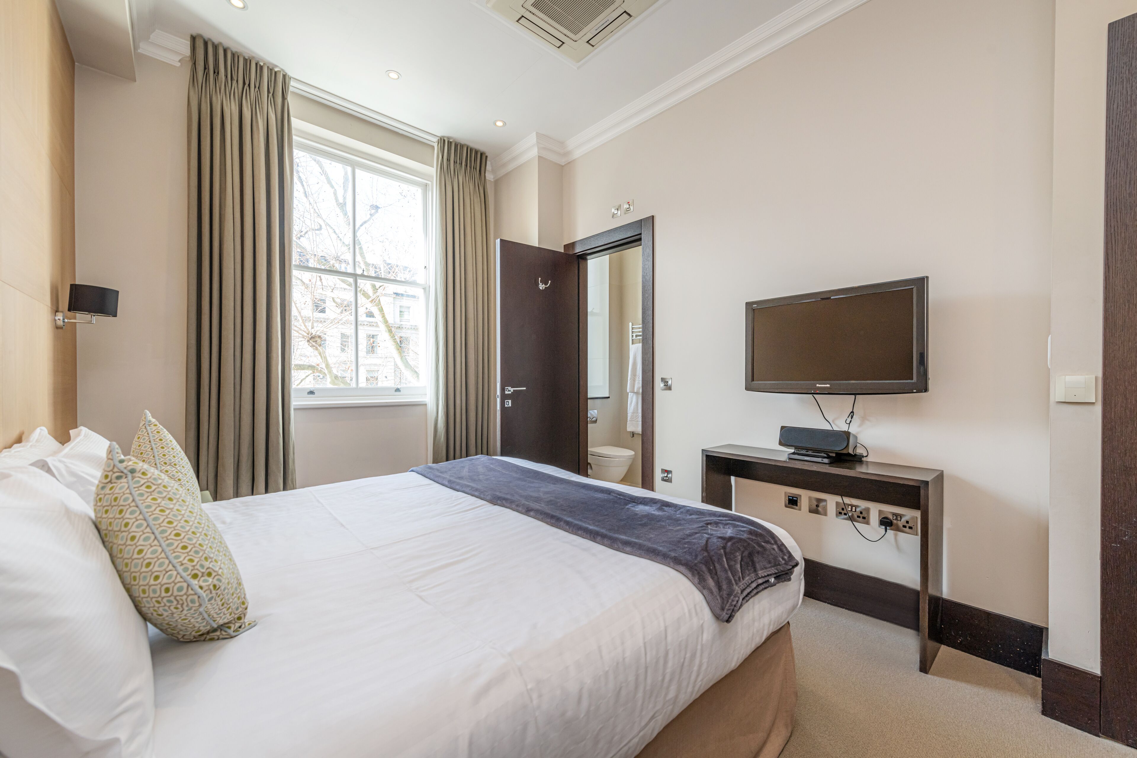 Ein Hotelzimmer mit Bett, Fernseher, Schreibtisch und einem Fenster mit Vorhängen.