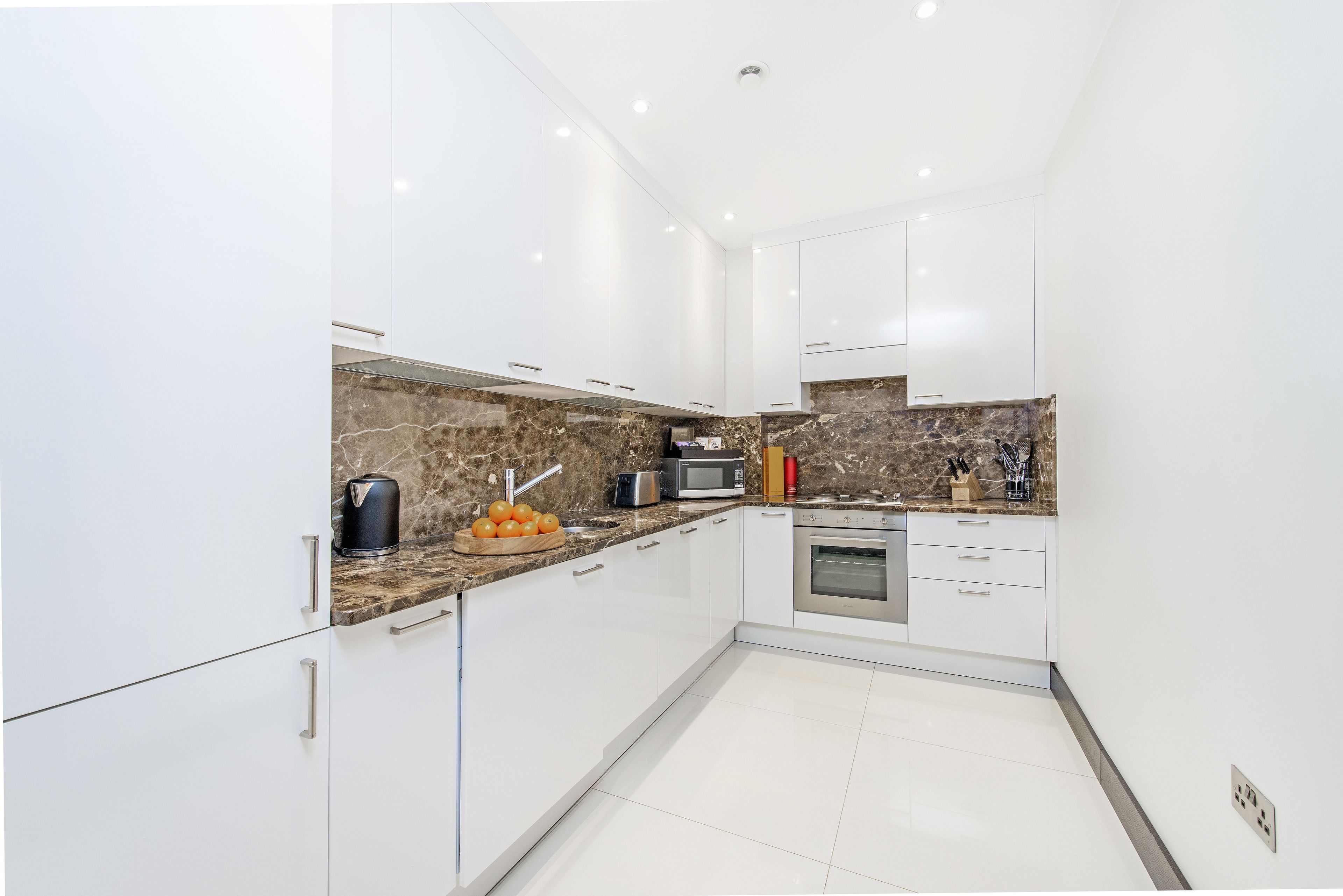 A modern kitchen with white cabinets, a marble backsplash, and stainless steel appliances.