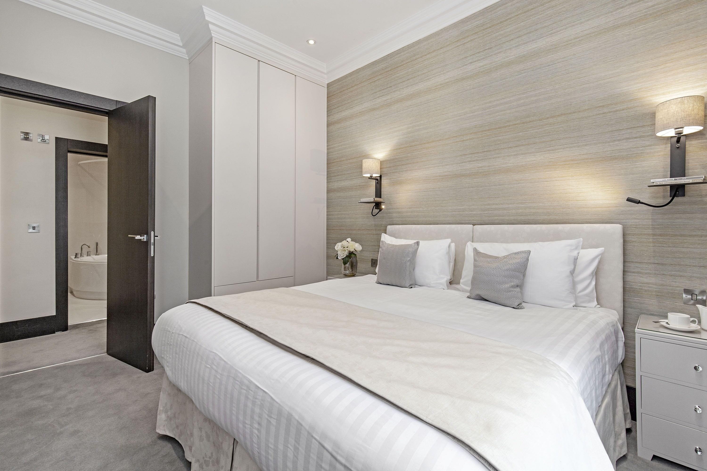 Une chambre à coucher moderne avec un grand lit, une table de chevet, une lampe fixée au mur et une porte donnant sur une salle de bain.