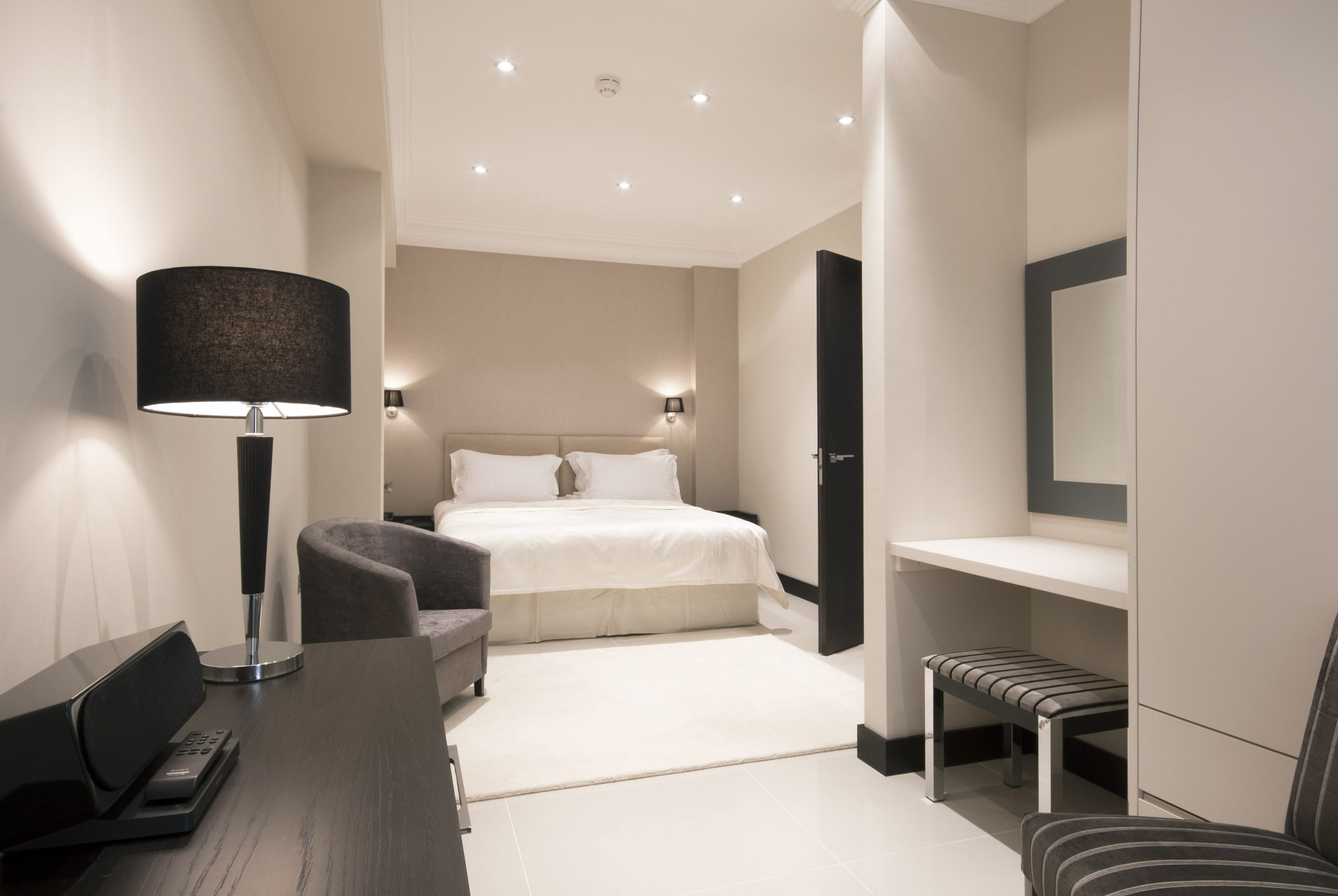 Una habitación de hotel moderna con cama, escritorio con lámpara, silla y banco.