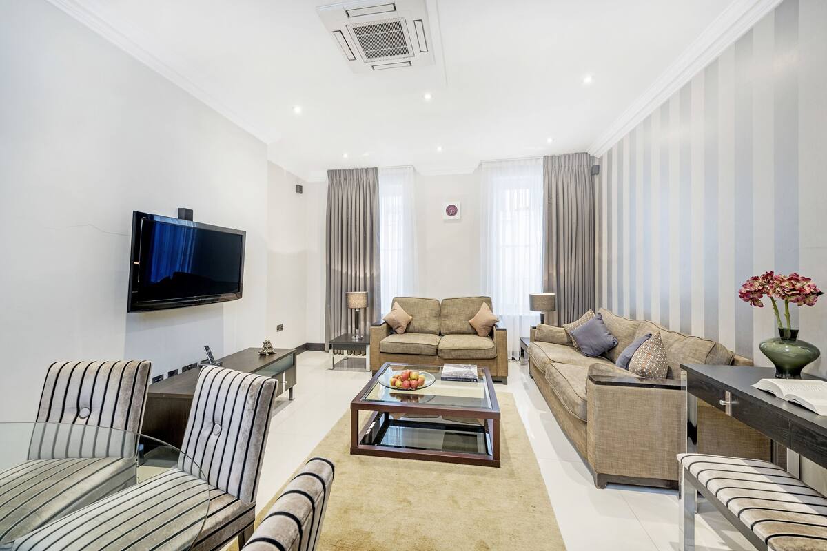 A modern living room with a flat-screen TV, two sofas, a coffee table with fruit, and a side table.