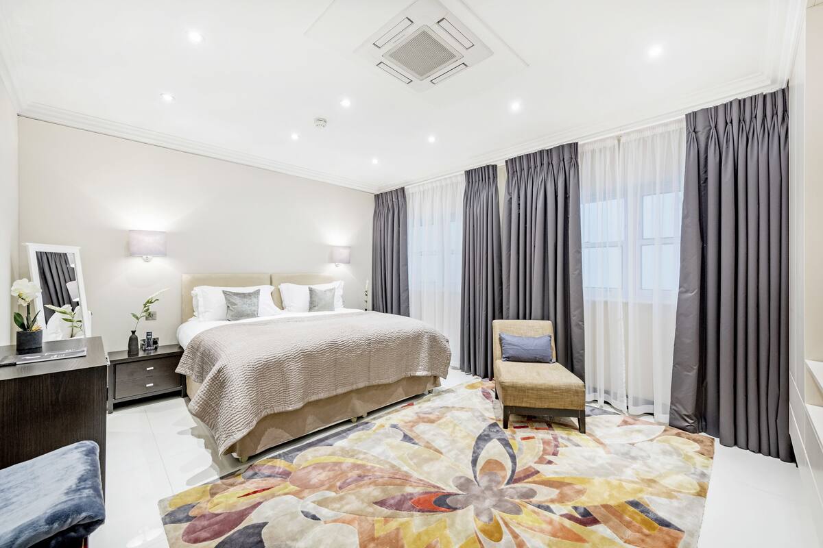 A modern bedroom with a large bed, bedside tables, a chair, and a decorative rug.
