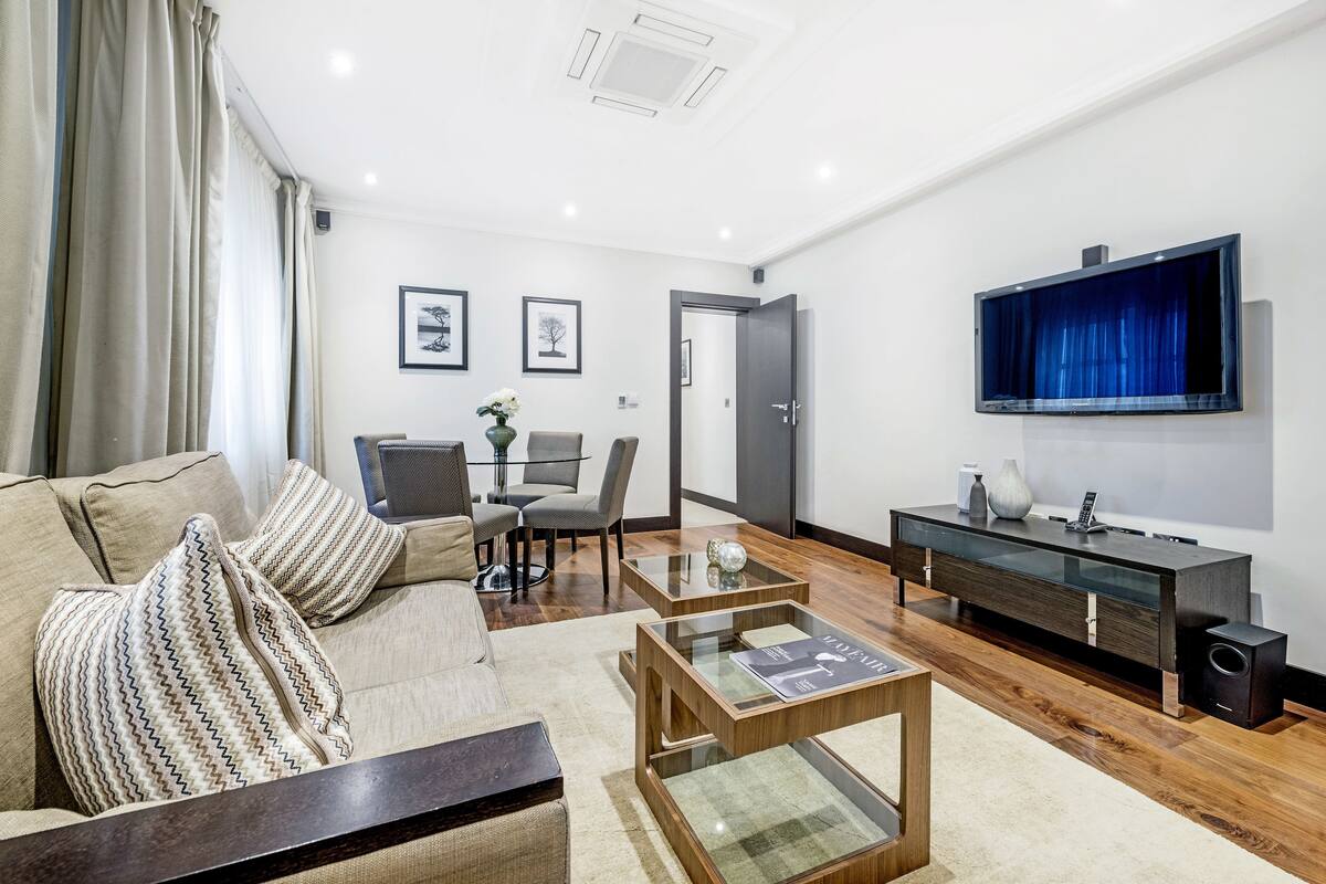 A modern living room with a sofa, coffee table, TV, and a dining area with chairs and a table.
