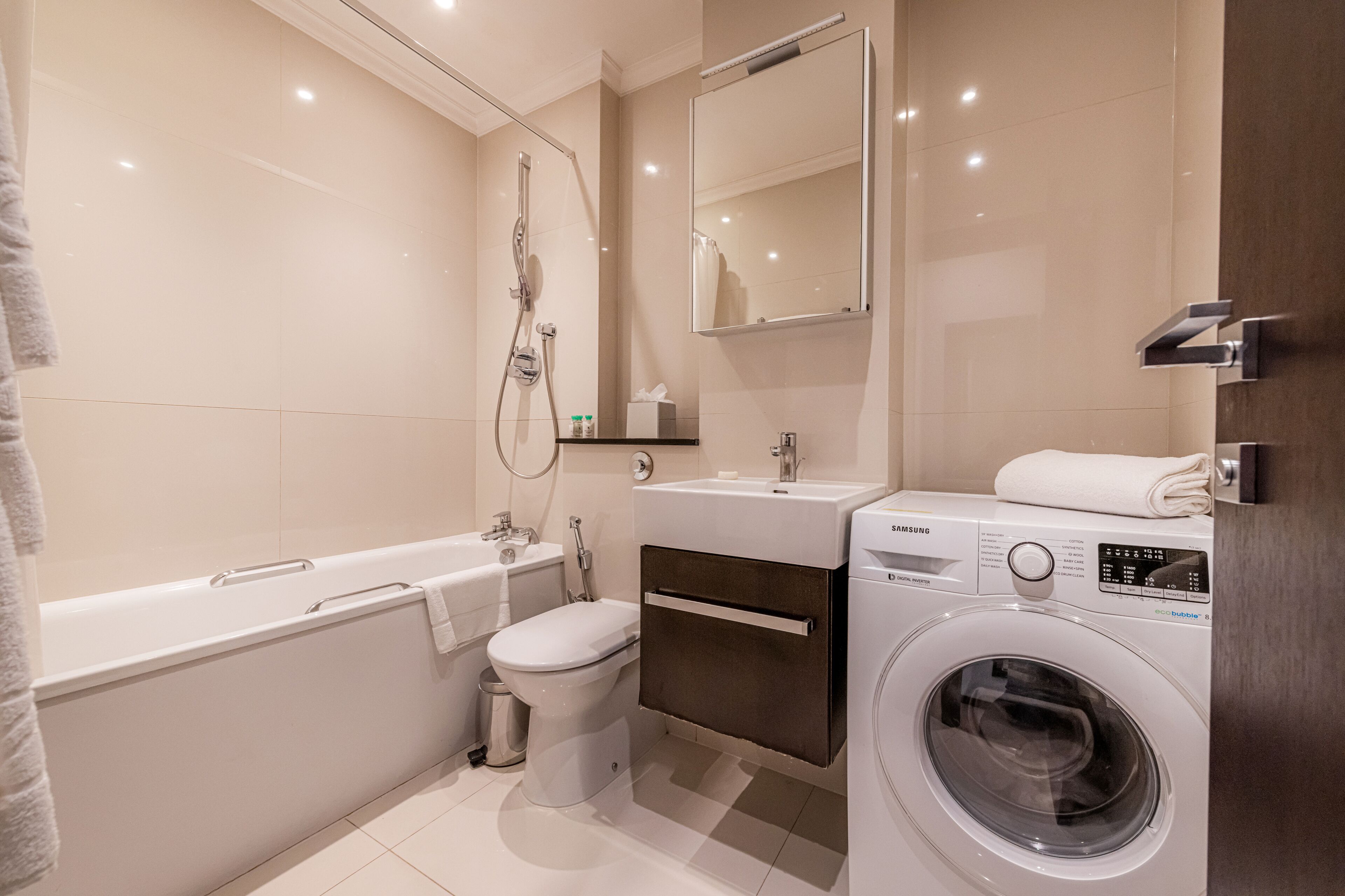 A modern bathroom with a bathtub, toilet, sink, and a front-loading washing machine.