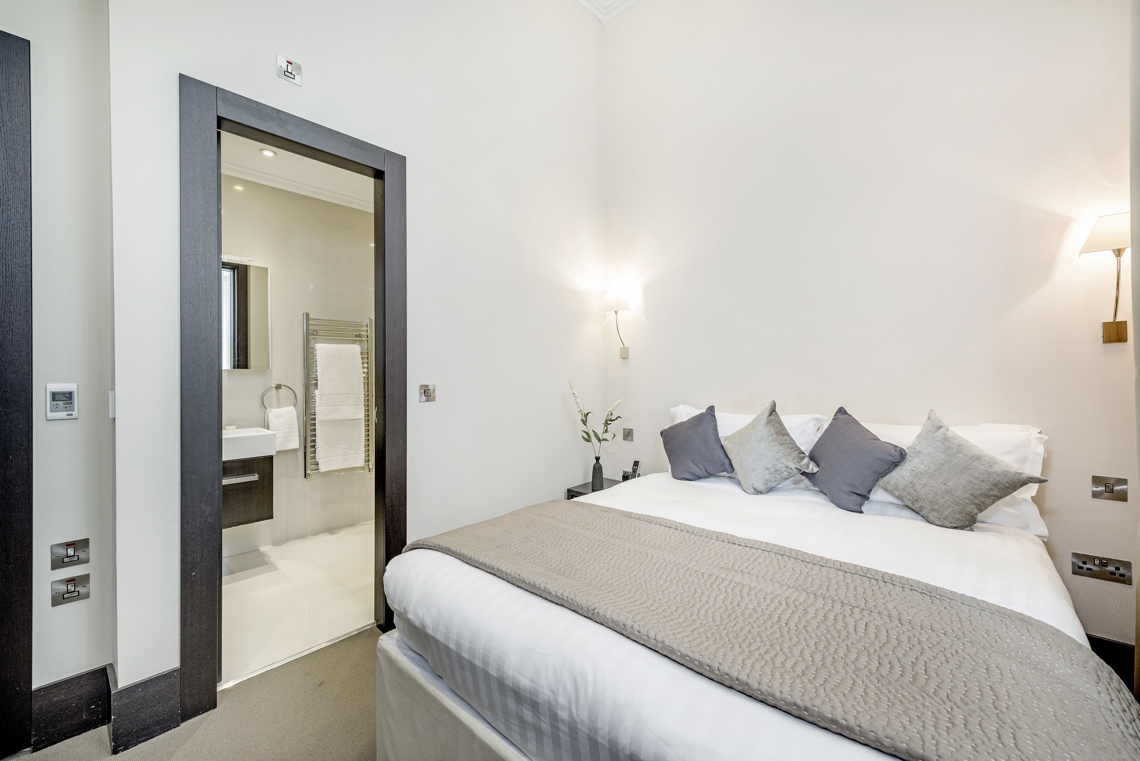 Una habitación de hotel moderna con una cama grande, una mesita de noche, un tocador y un baño visible a través de una puerta abierta.