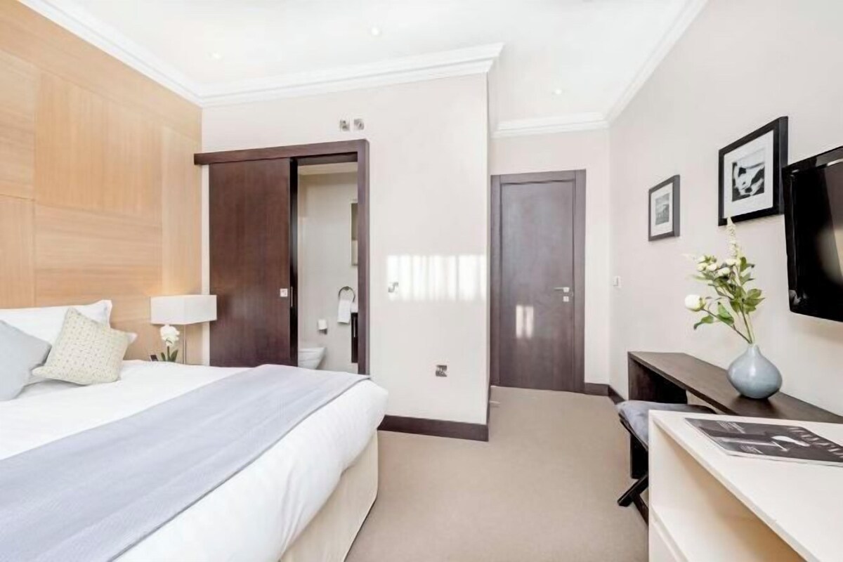 Une chambre d’hôtel avec un grand lit, un bureau, une chaise, une télévision et une porte donnant sur une salle de bain.