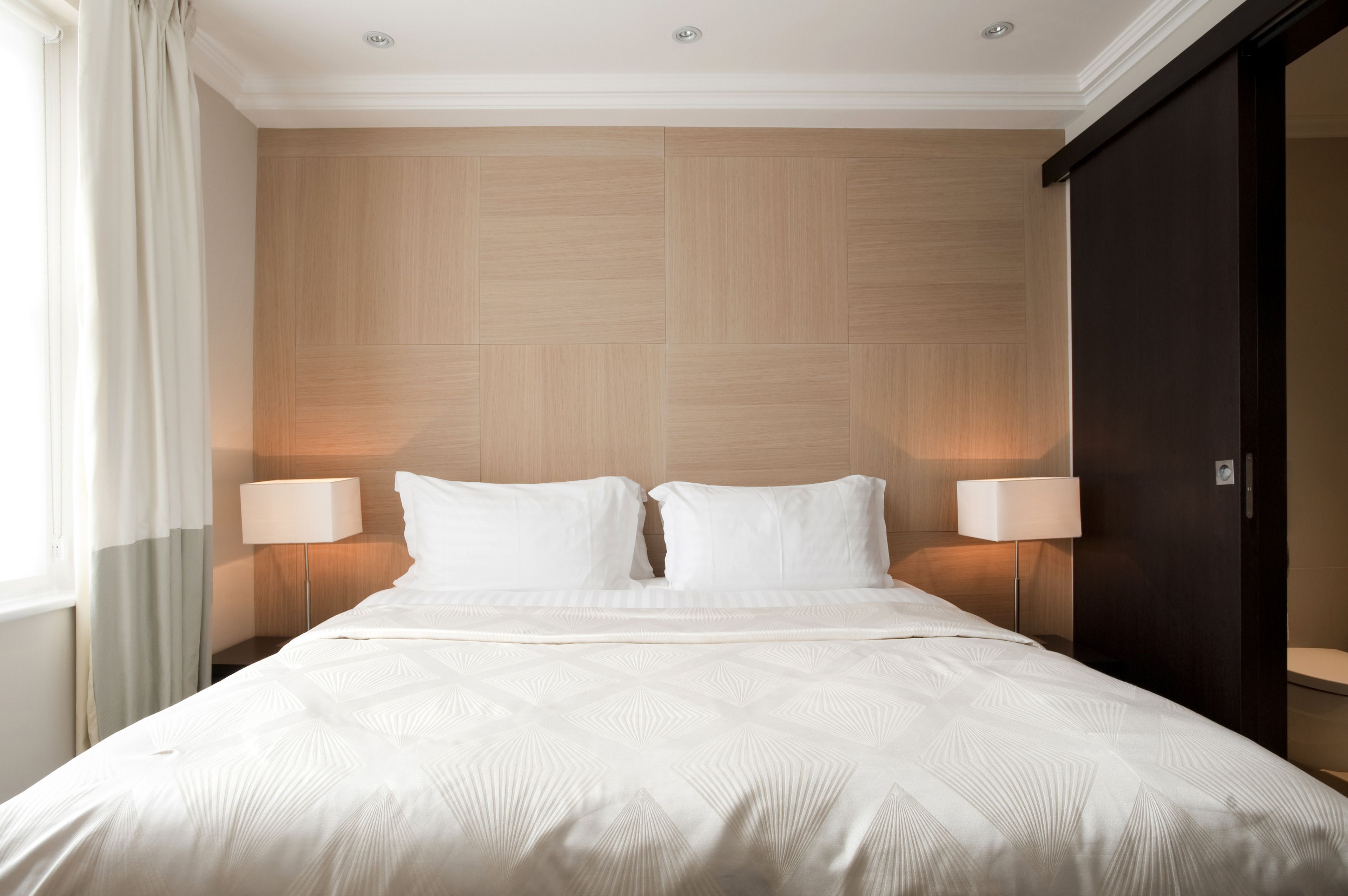 A hotel room with a large bed, two bedside lamps, a wooden headboard, and a dark wardrobe.